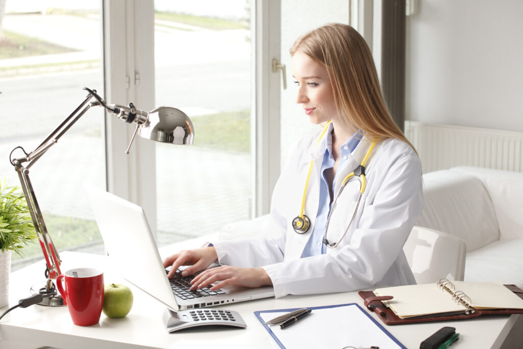 Side view of a female medical professional using a laptop at her desk, showcasing the technological skills that determine how much do medical billing and coding make in the AI era.